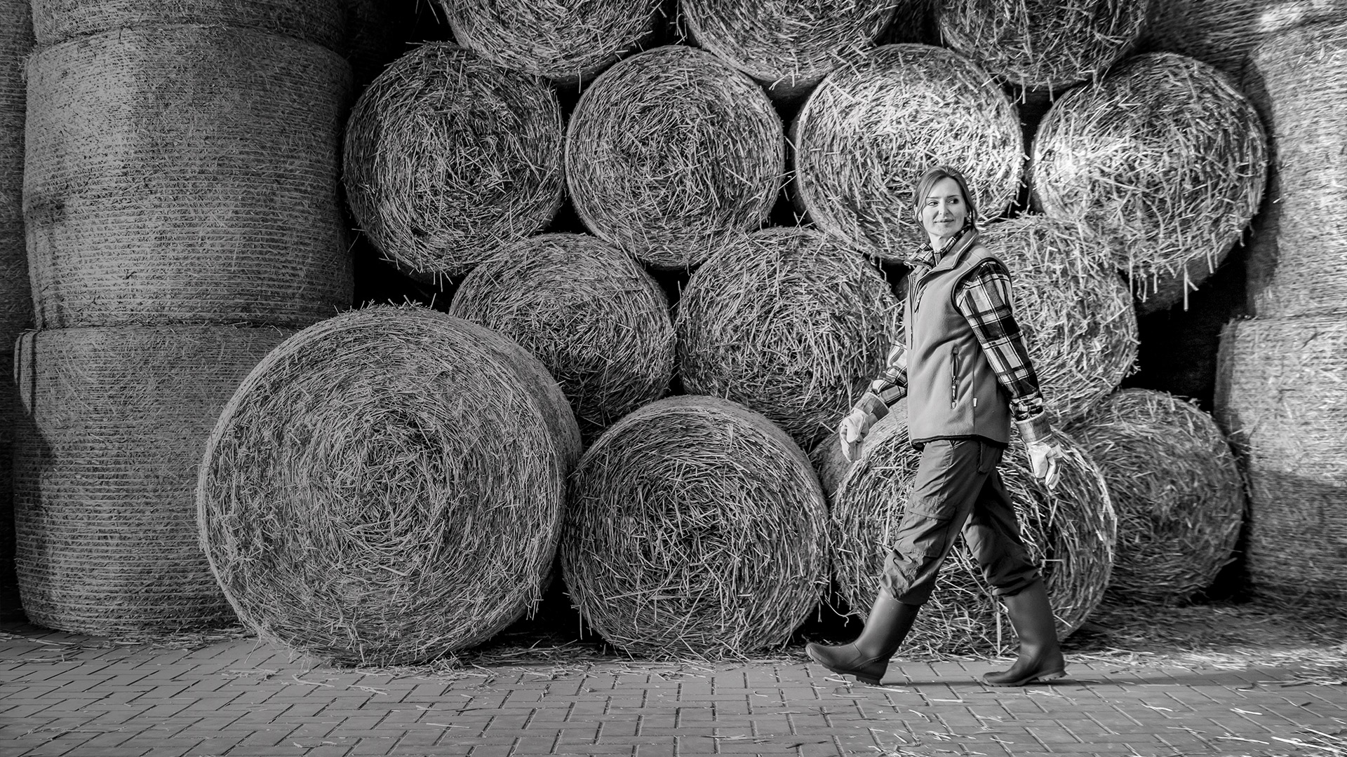 Female Farmer walking infront of hay bales